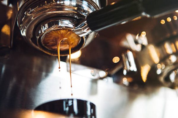 Fresh and hot espresso coffee pours from a portafilter on a nice chrome espresso machine.  Horizontal image with copy space.
